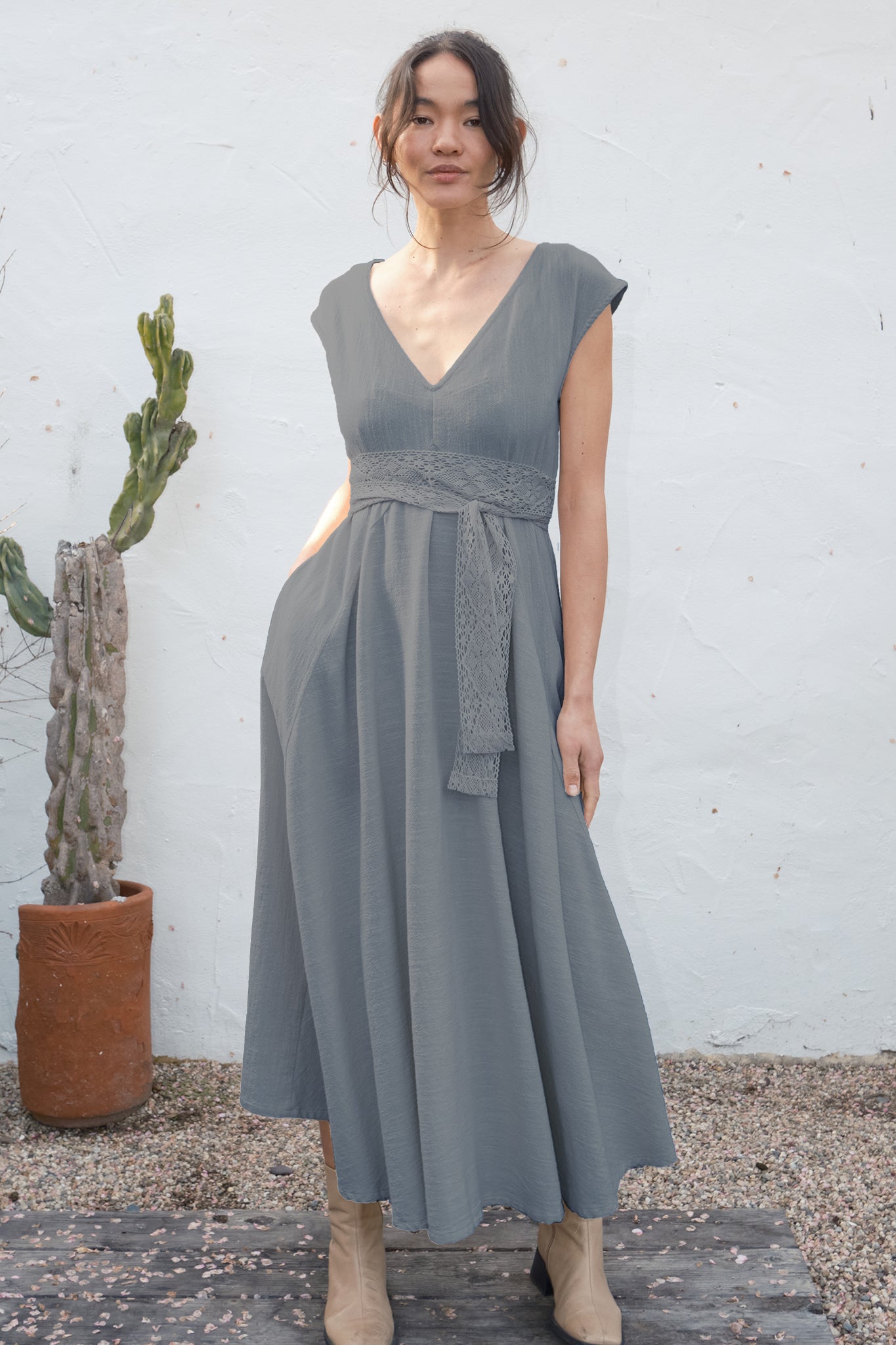 Woman wearing a gray dress standing against a white wall with a cactus plant.