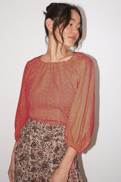Woman wearing a vermillion blouse with floral patterned skirt against a white background