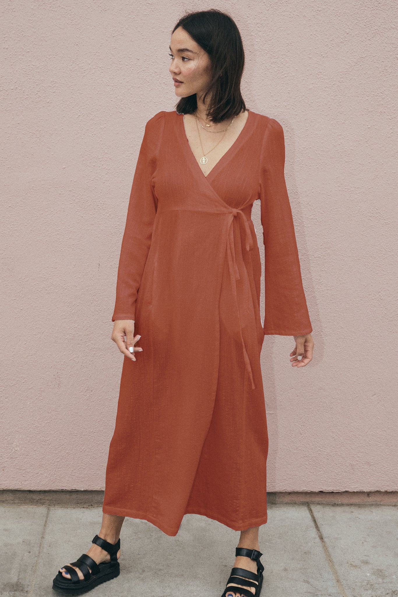 Woman wearing a rust-colored dress against a pink wall.