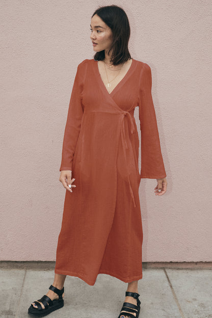 Woman wearing a rust-colored dress against a pink wall.