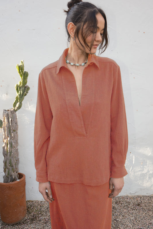 Woman wearing a persimmon colored outfit standing against a white wall with a cactus plant.