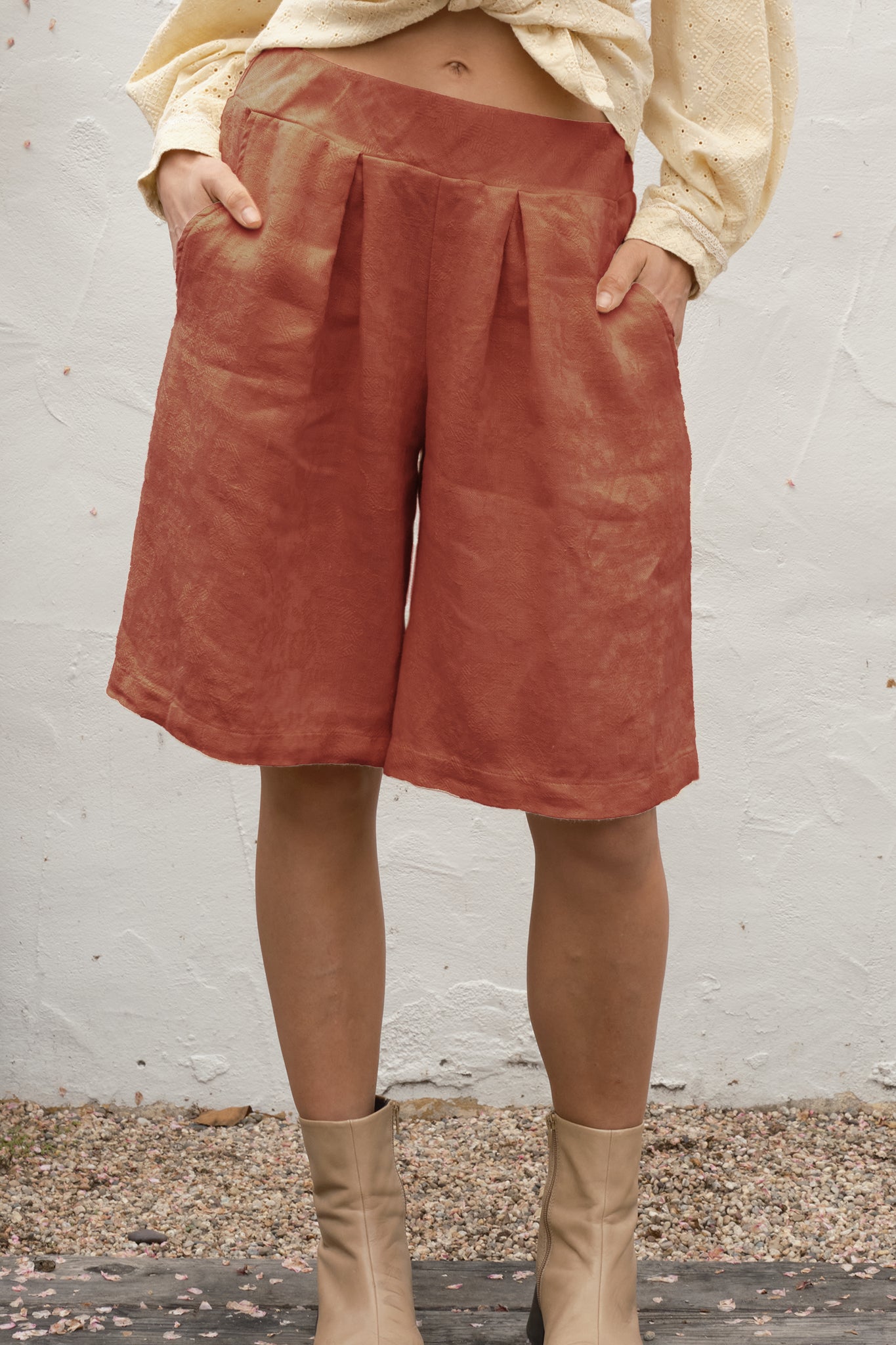 Person wearing rust-colored shorts and beige boots against a white wall.