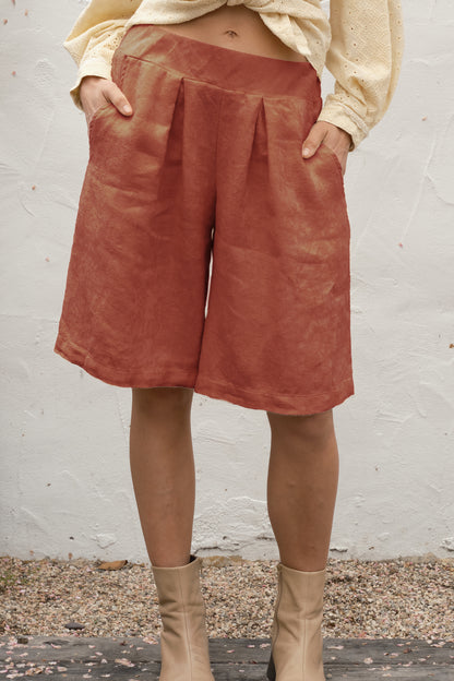 Person wearing rust-colored shorts and beige boots against a white wall.