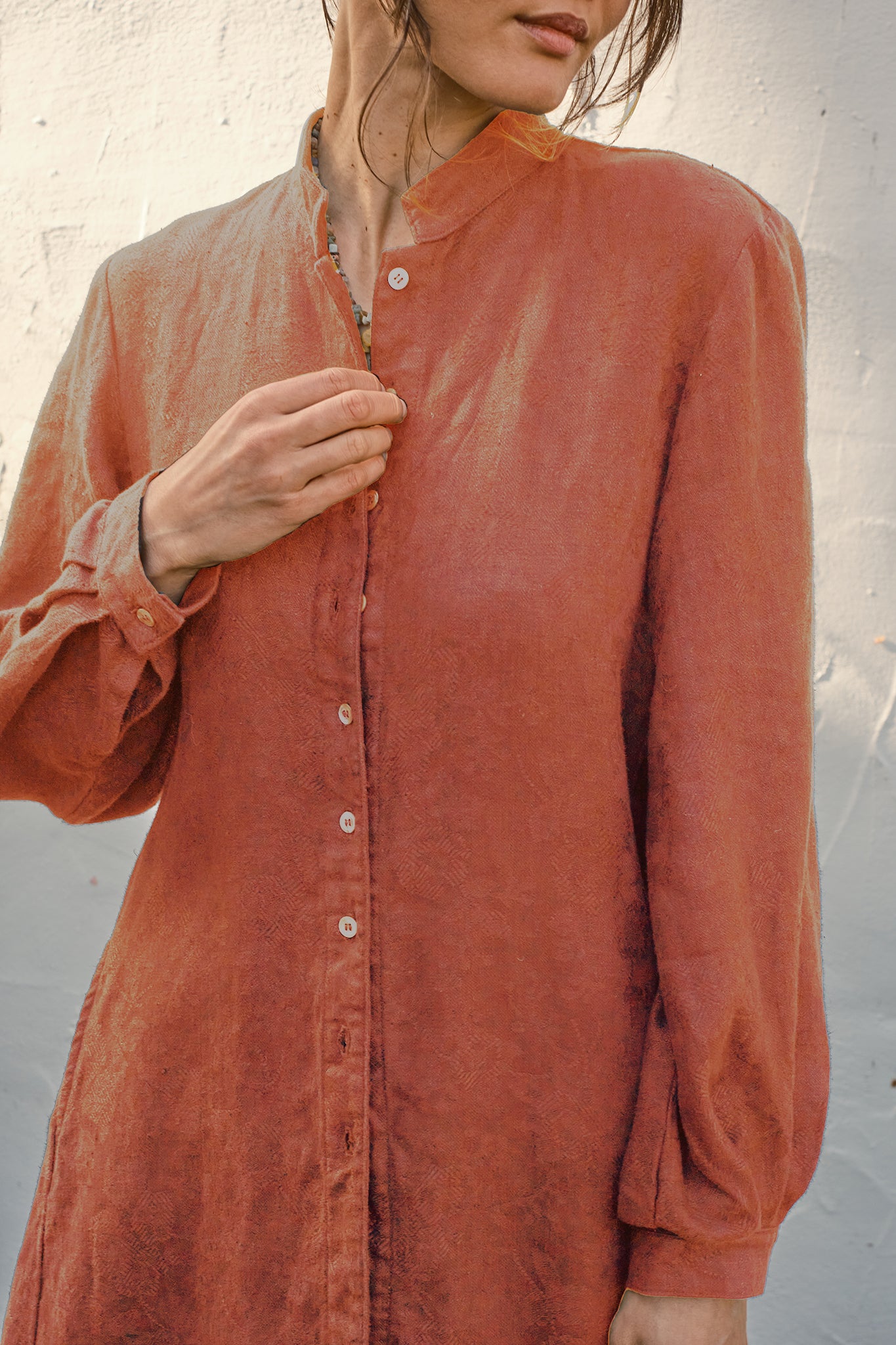 Person wearing a rust-colored long-sleeve  damask coat against a neutral background