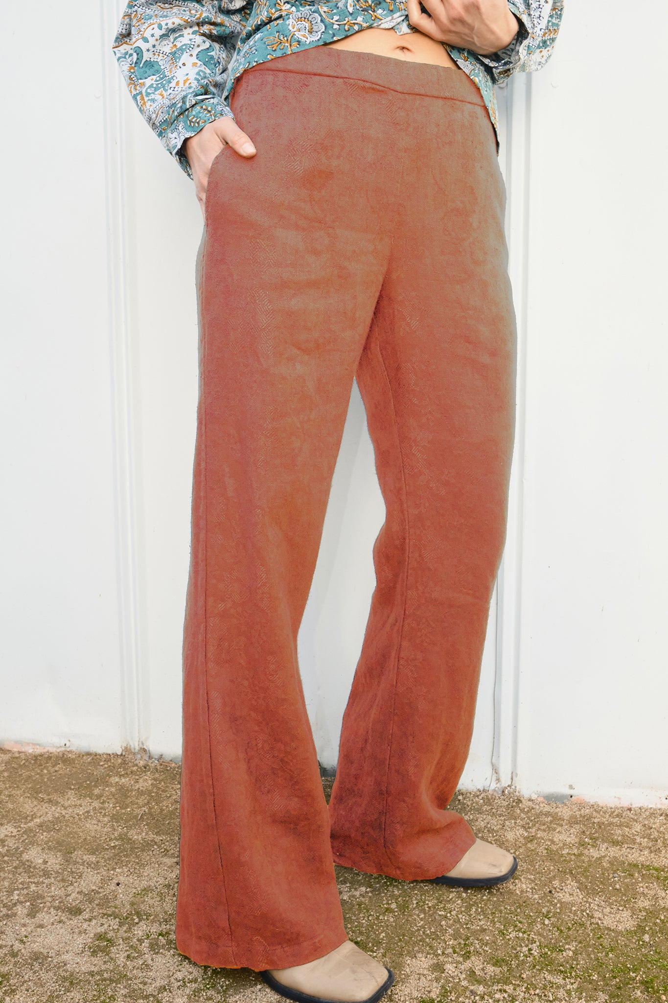 Person wearing persimmon flared pants against a white wall.