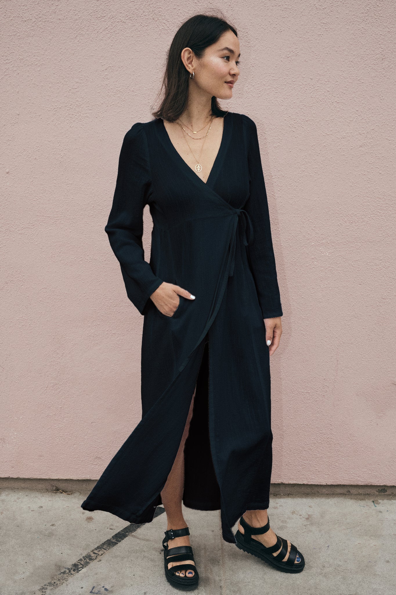 Woman wearing a black wrap dress against a pink wall