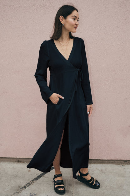 Woman wearing a black wrap dress against a pink wall