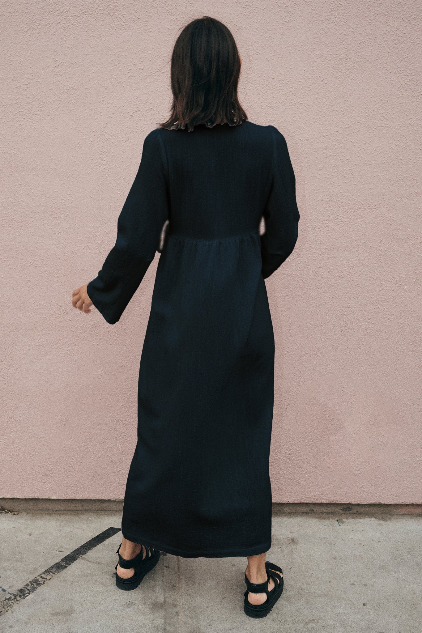 Person wearing a black dress against a pink wall