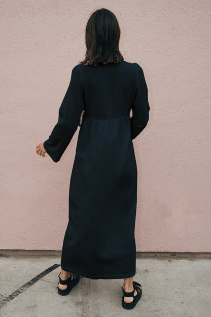 Person wearing a black dress against a pink wall