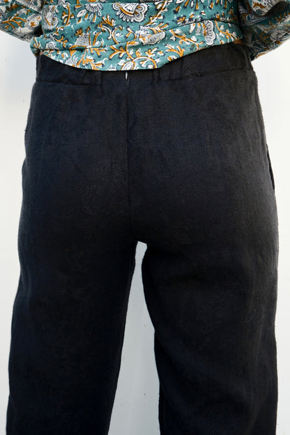 Black pants worn with a patterned shirt on a white background . back view