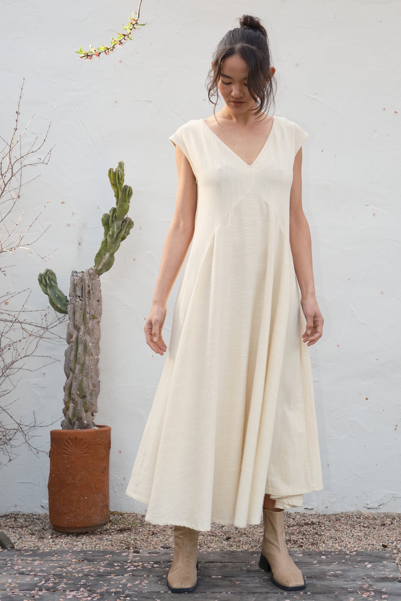Woman wearing a beige dress standing against a white wall with a cactus plant.