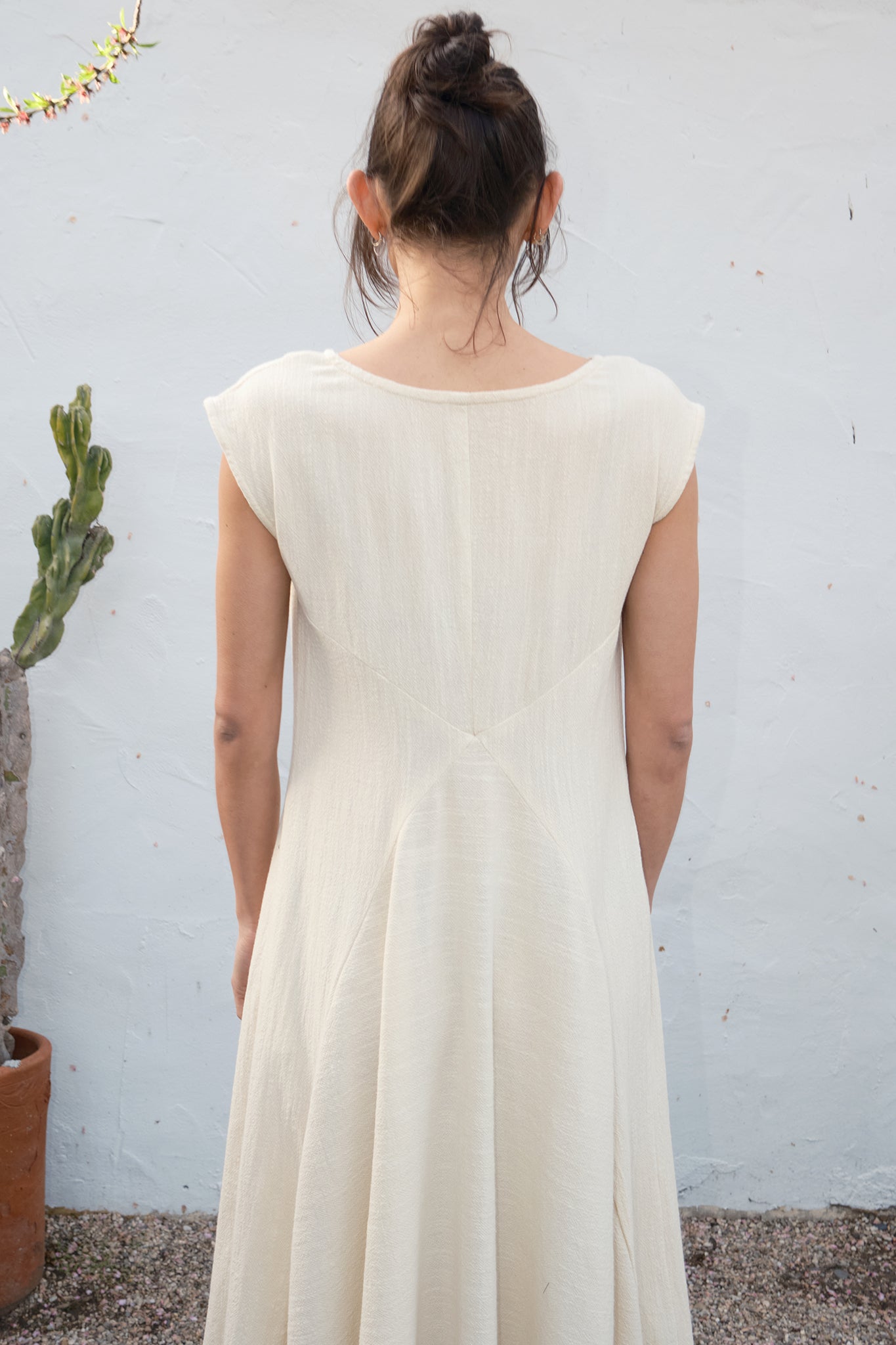 Person wearing an alabaster dress standing against a light gray wall with a plant in the background.