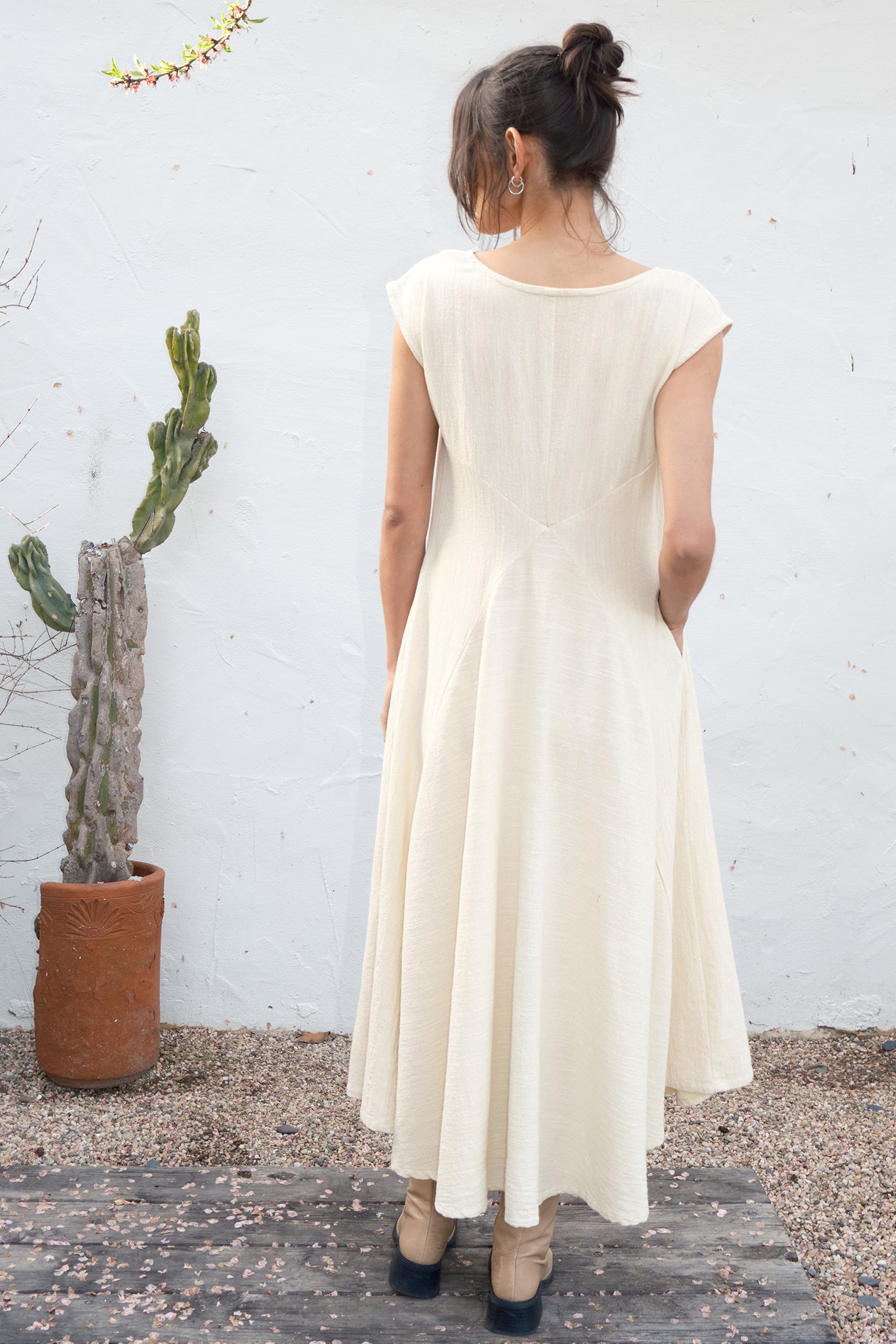 Woman wearing an alabaster dress standing in front of a white wall with a cactus plant.