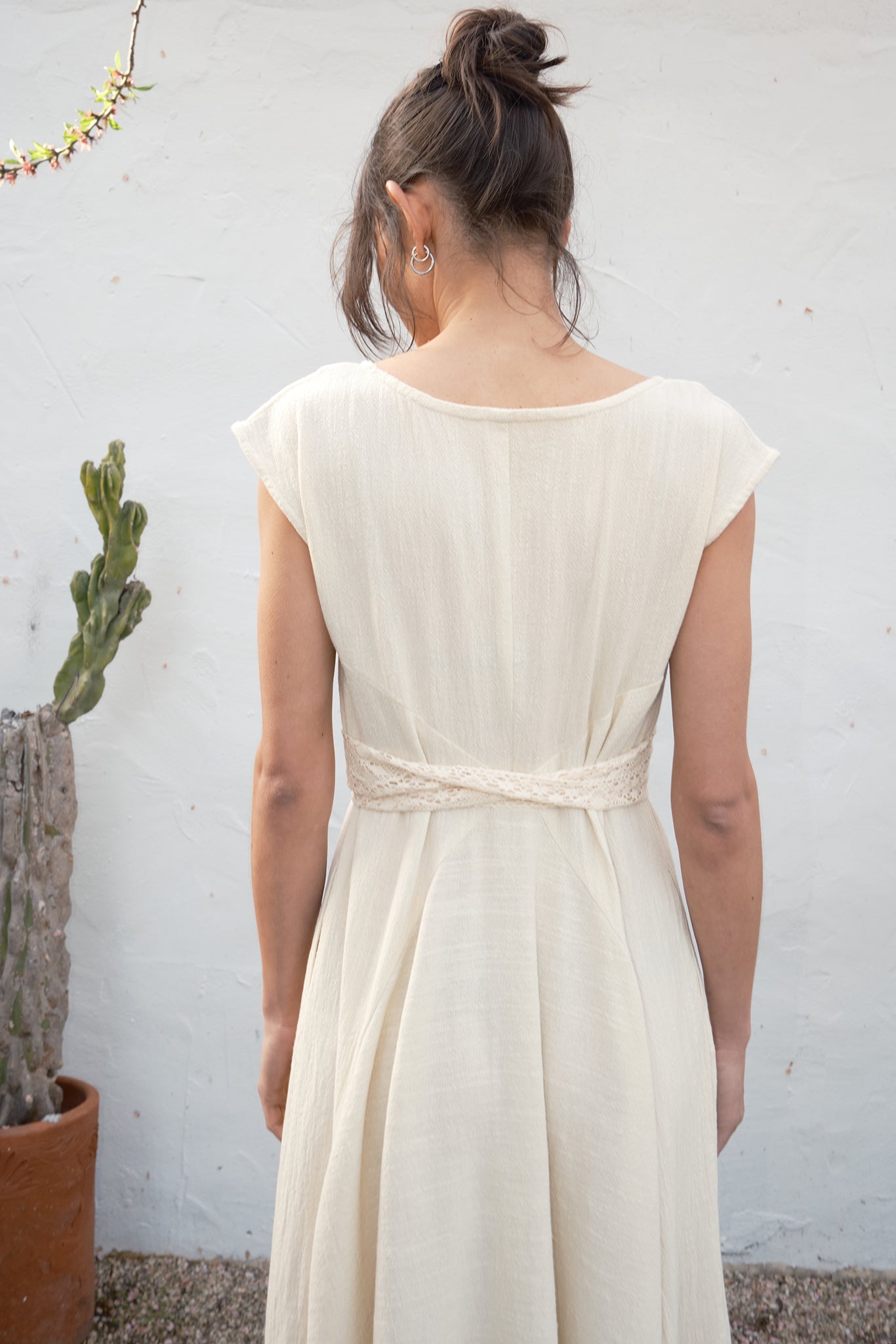 Woman wearing an alabaster dress against a plain wall with a plant in the background